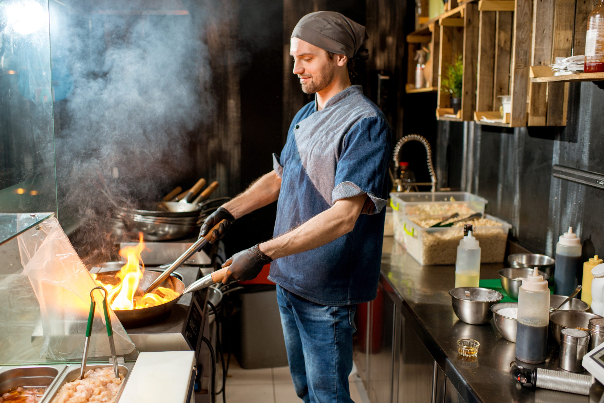 Caucasian chief cook cooking with wok pan on the asian restaurant kitchen