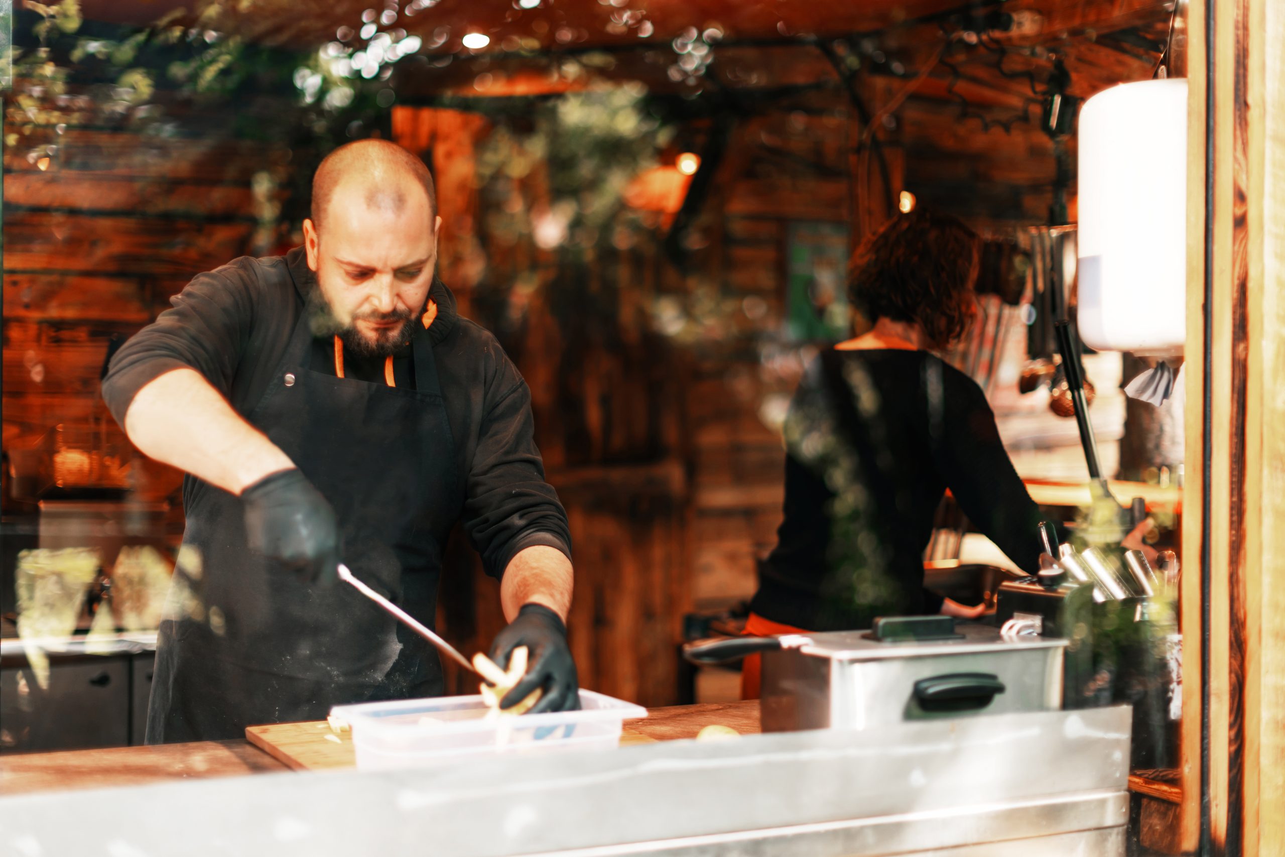 Photo taken from outside through the kitchen glass of a steakhouse chef preparing giant skewers