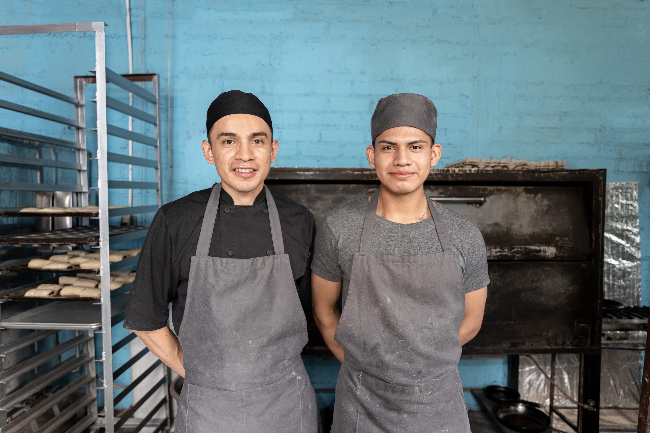 Portrait of two young Hispanic bakers posing in front of the bakery oven. Concept of traditional Mexican sweet bread craft